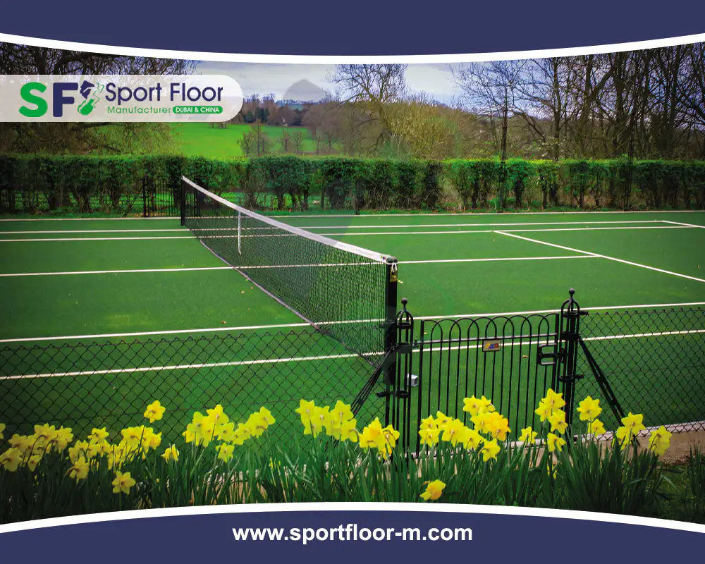 Green outdoor tennis court with perimeter fencing and landscaping